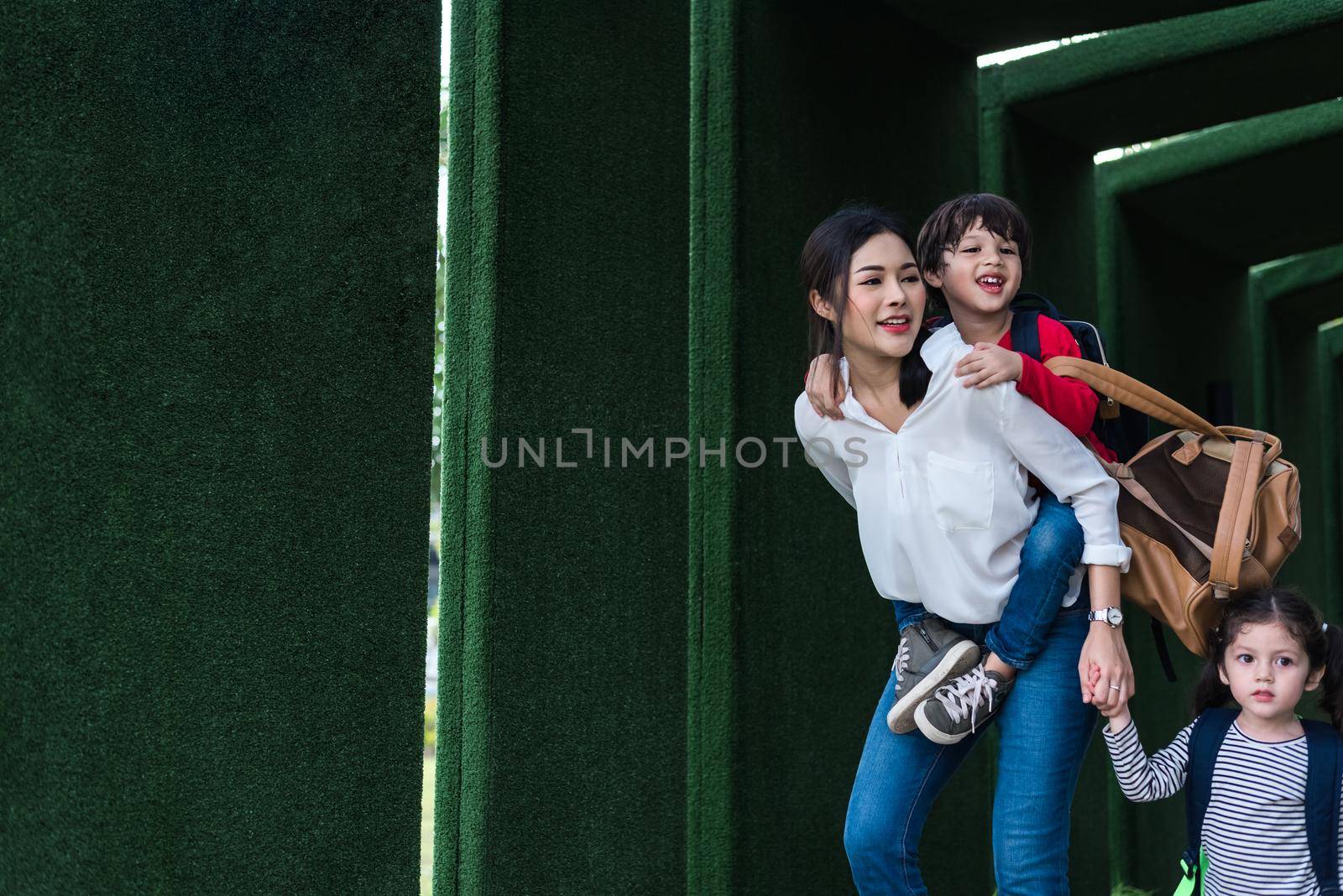 Single mom carrying and playing with her children in garden with green wall background. People and Lifestyles concept. Happy family and Home sweet home theme. Outdoors and nature theme.