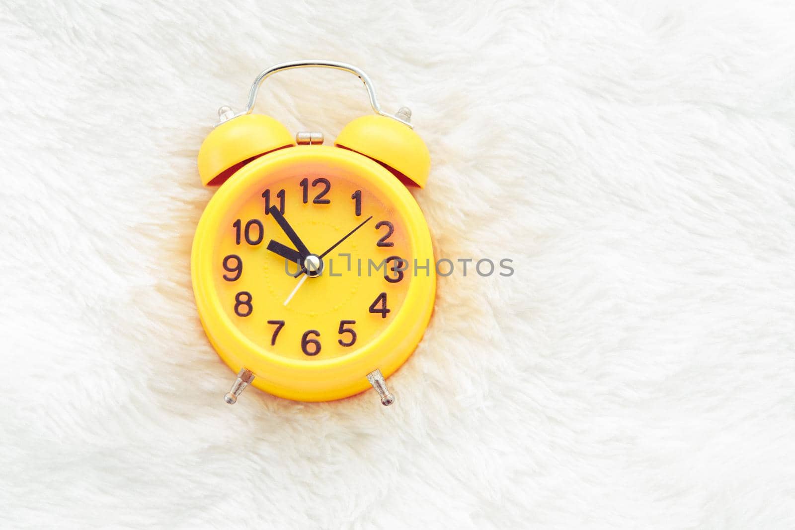 Yellow alarm clock on white wool. Late and Lazy time concept. Morning in holiday theme. Around 10 O Clock