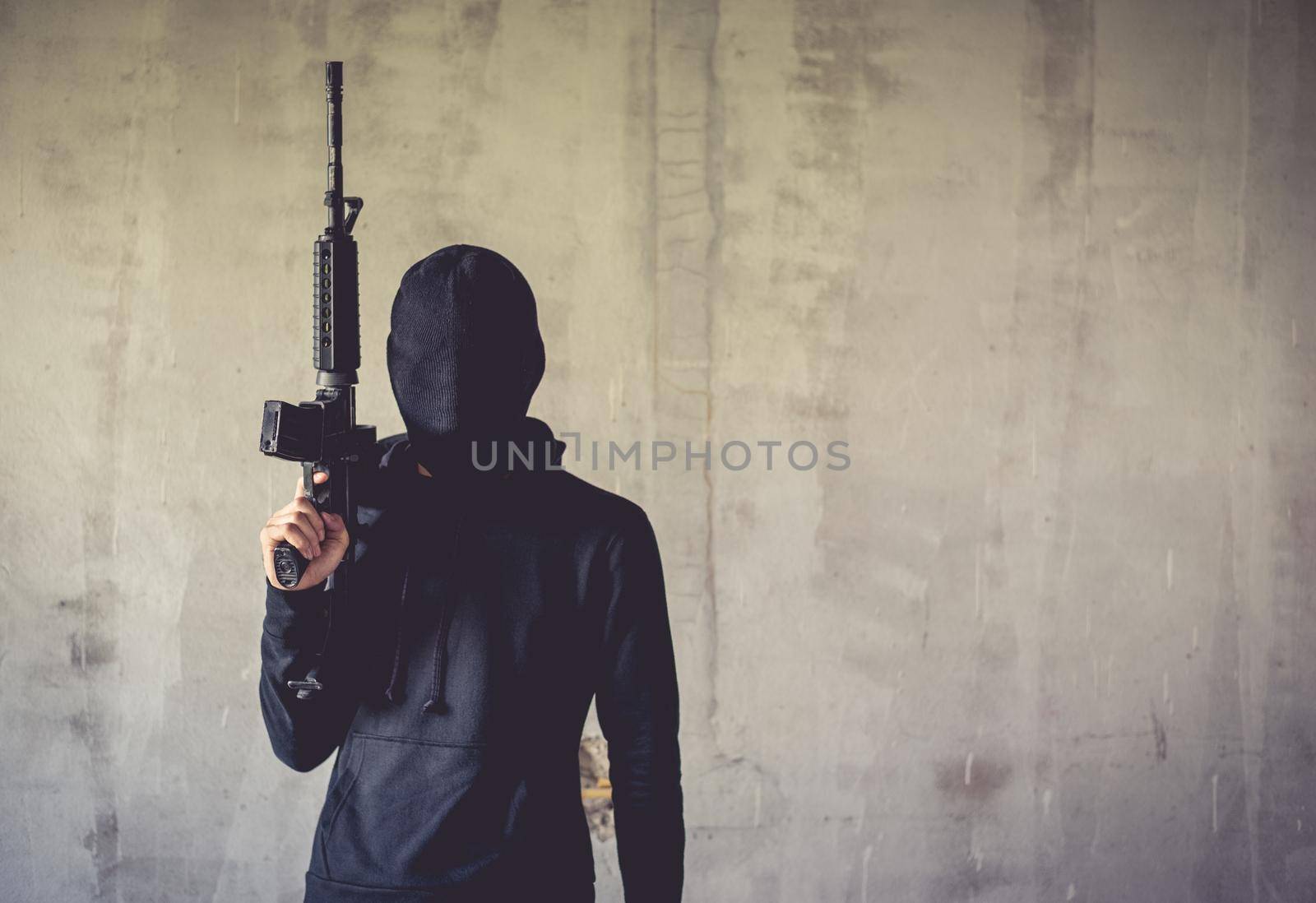 Terrorist holding rifle gun on grunge wall. Social issued theme. Terrorist and Robber concept. Police and Soldier theme. Social issued theme.