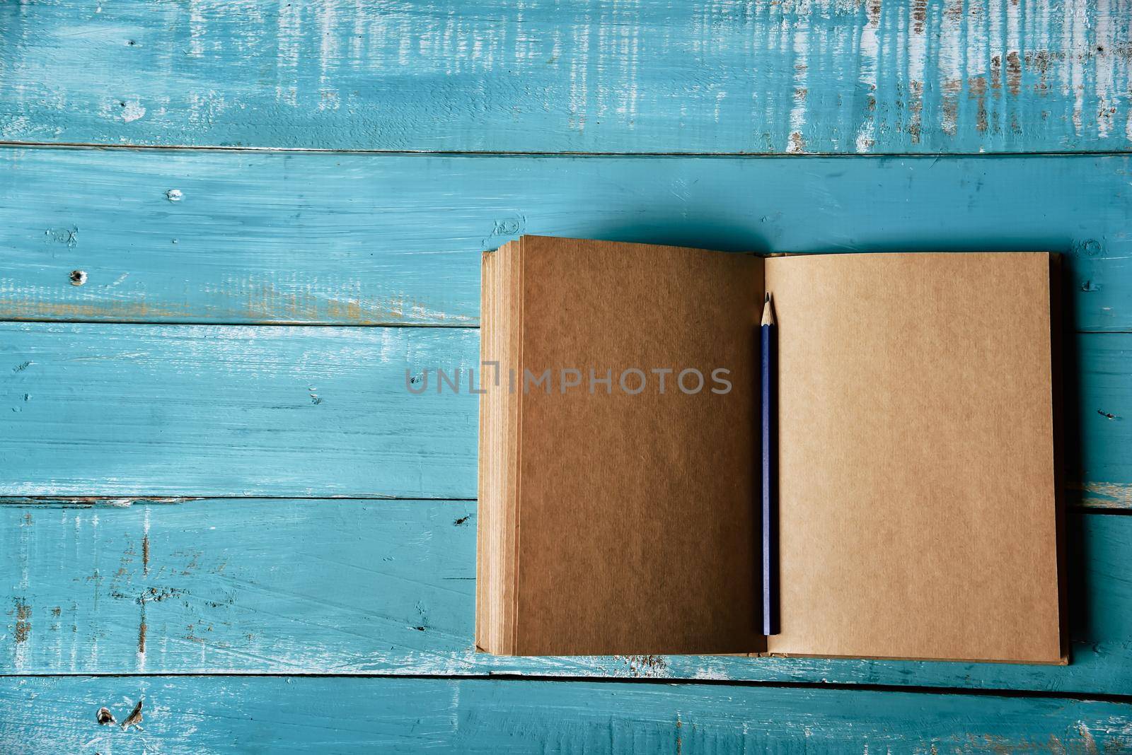 Top view of blank open notebook on blue wooden background with purple pencil in middle. Working stationery office. Education and Business concept. Minimal and Flat lay theme. Copy space on left