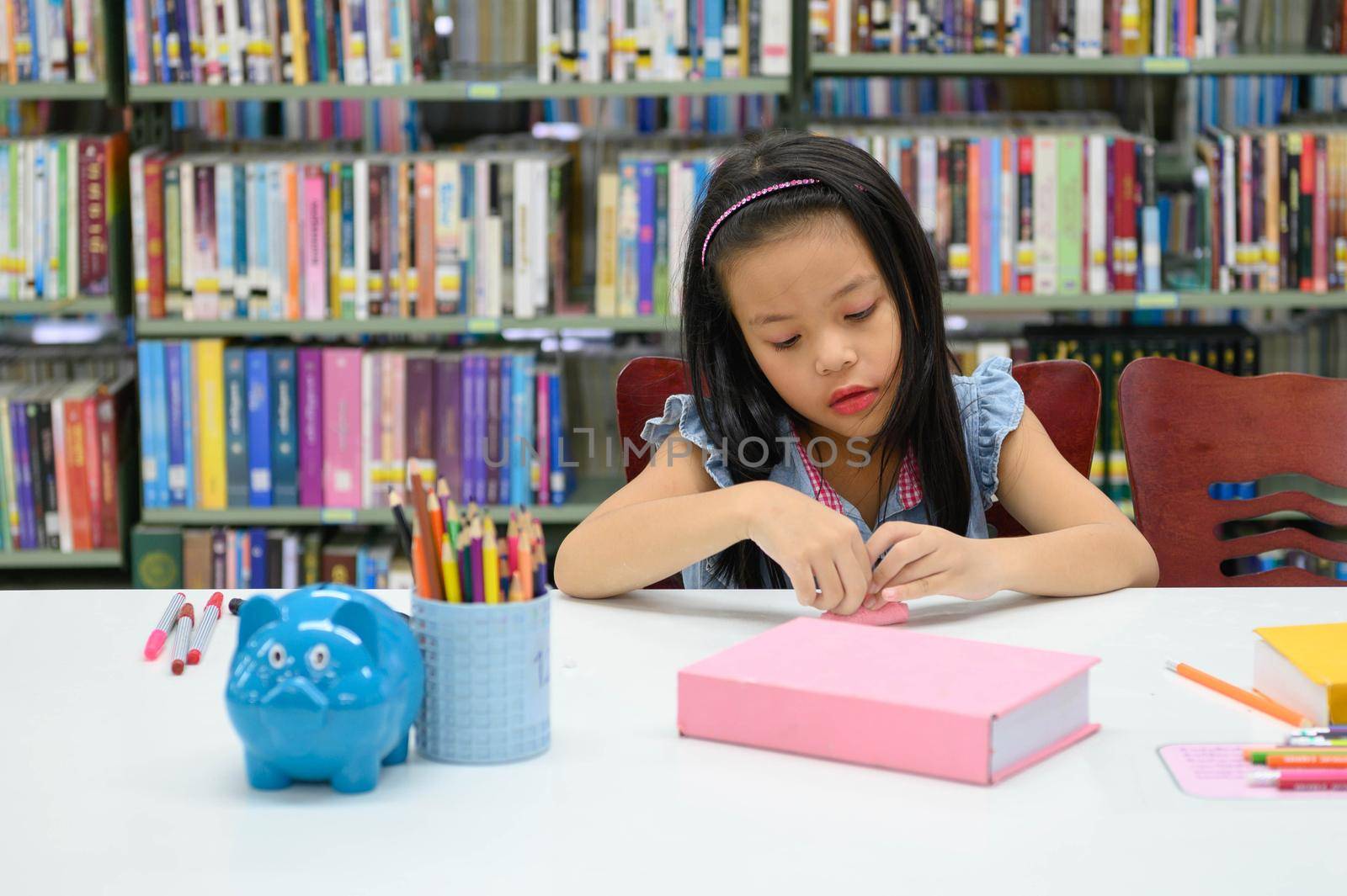 Asian girl folding and crafting paper in library during art class. Education and activity concept
