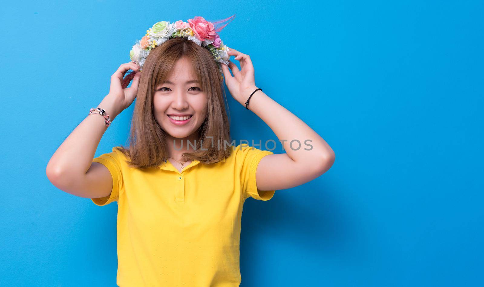 Beauty woman posing with flower hat in front of blue wall background. Summer and vintage concept. Happiness lifestyle and people portrait theme. Cute gesture and pastel tone.