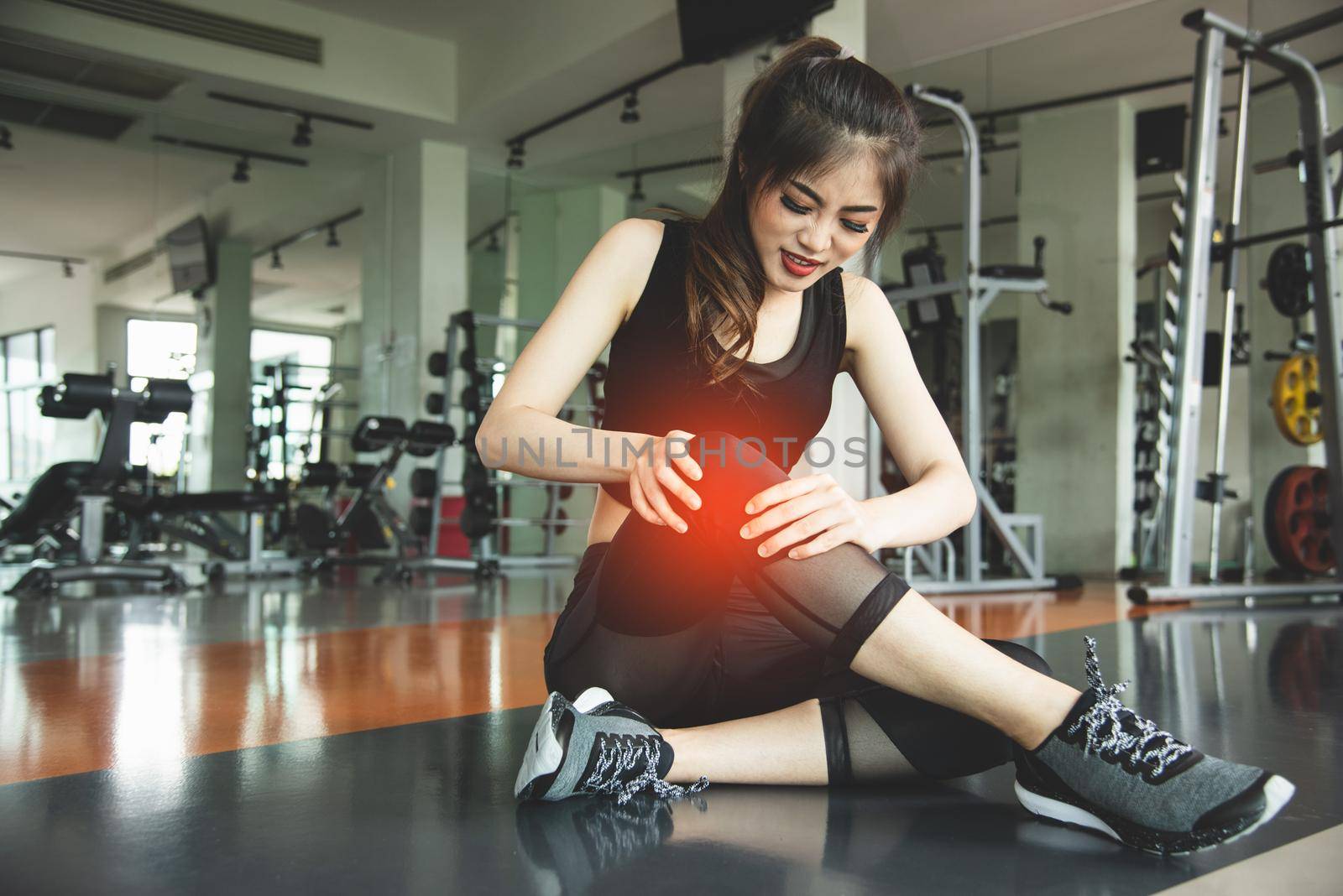 Asian woman injuries during workout at knee in fitness gym sport center. Medical and Healthcare concept. Exercise and Training theme. People healthy lifestyle and leisure activity problem