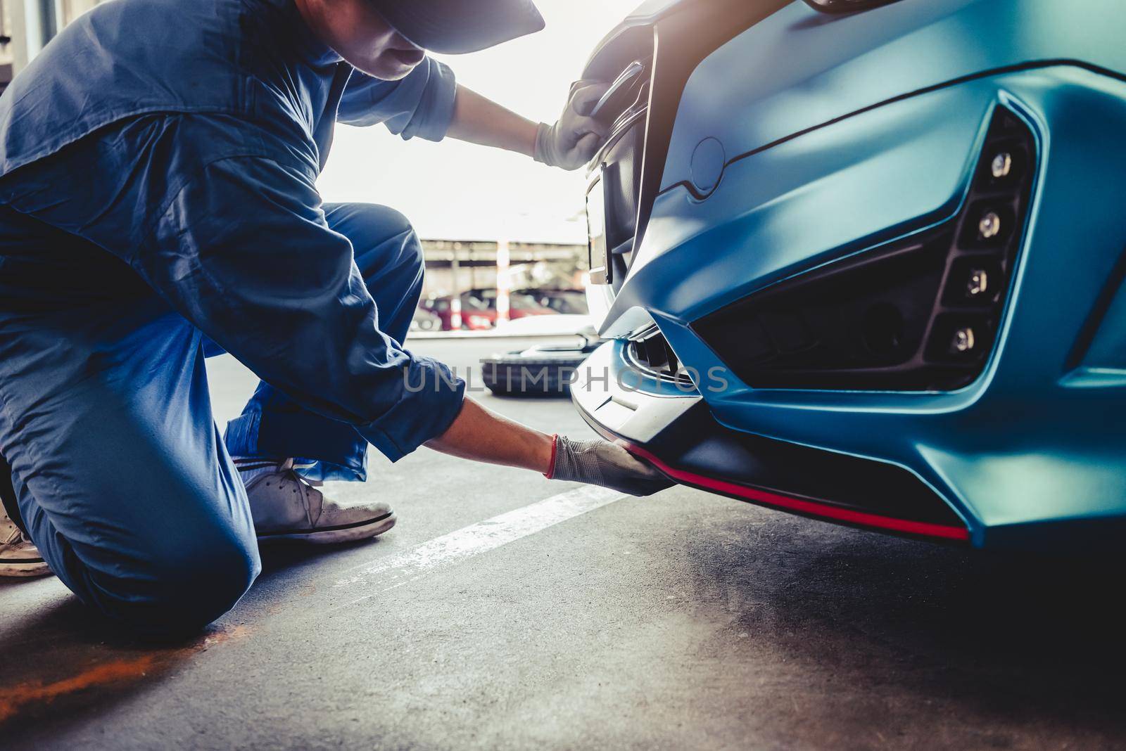 Mechanics installing front skirt at auto repair shop garage. Transportation and Business concept. Automobile technician maintenance vehicle by customer claim order. Car salon accessories decoration