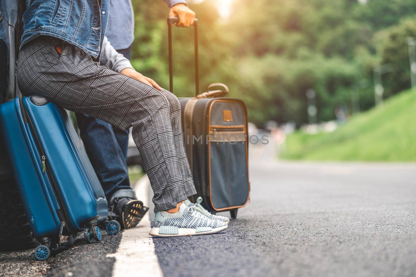 Closeup lower body of Asian couple relaxing on SUV car trunk with yellow trolley luggage along road trip with mountain hill background. Freedom road life. People lifestyle and transportation travel
