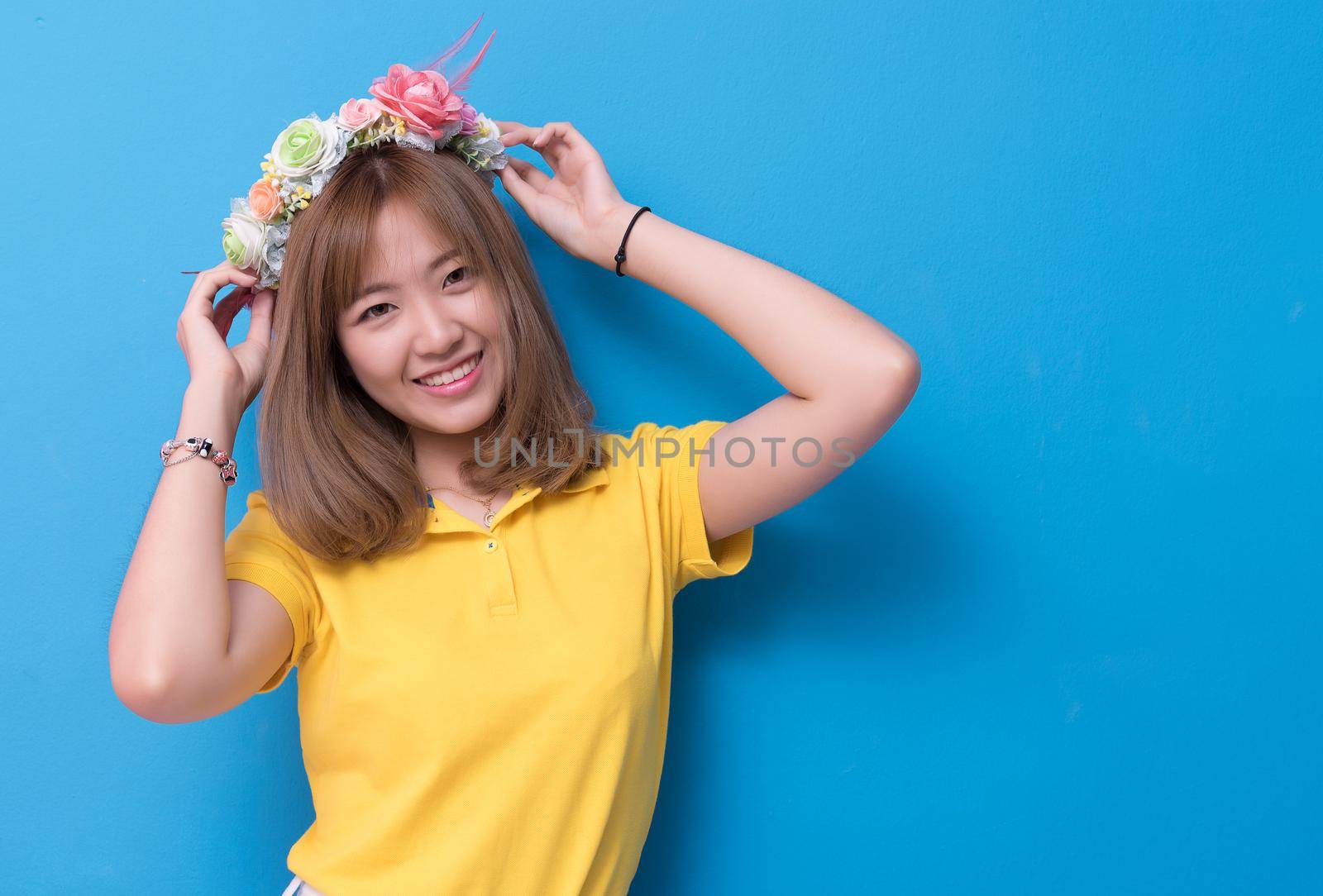 Beauty woman posing with flower hat in front of blue wall background. Summer and vintage concept. Happiness lifestyle and people portrait theme. Cute gesture and pastel tone.