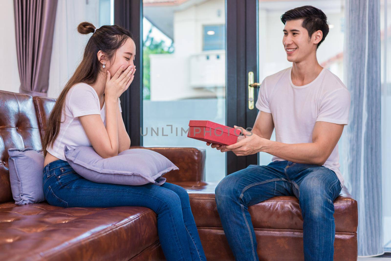 Boyfriend surprising girlfriend with present. Woman surprised when looking at gift box on special day. Lovers and Couples concept. Honeymoon and Dating theme. Happiness and Valentines day theme.