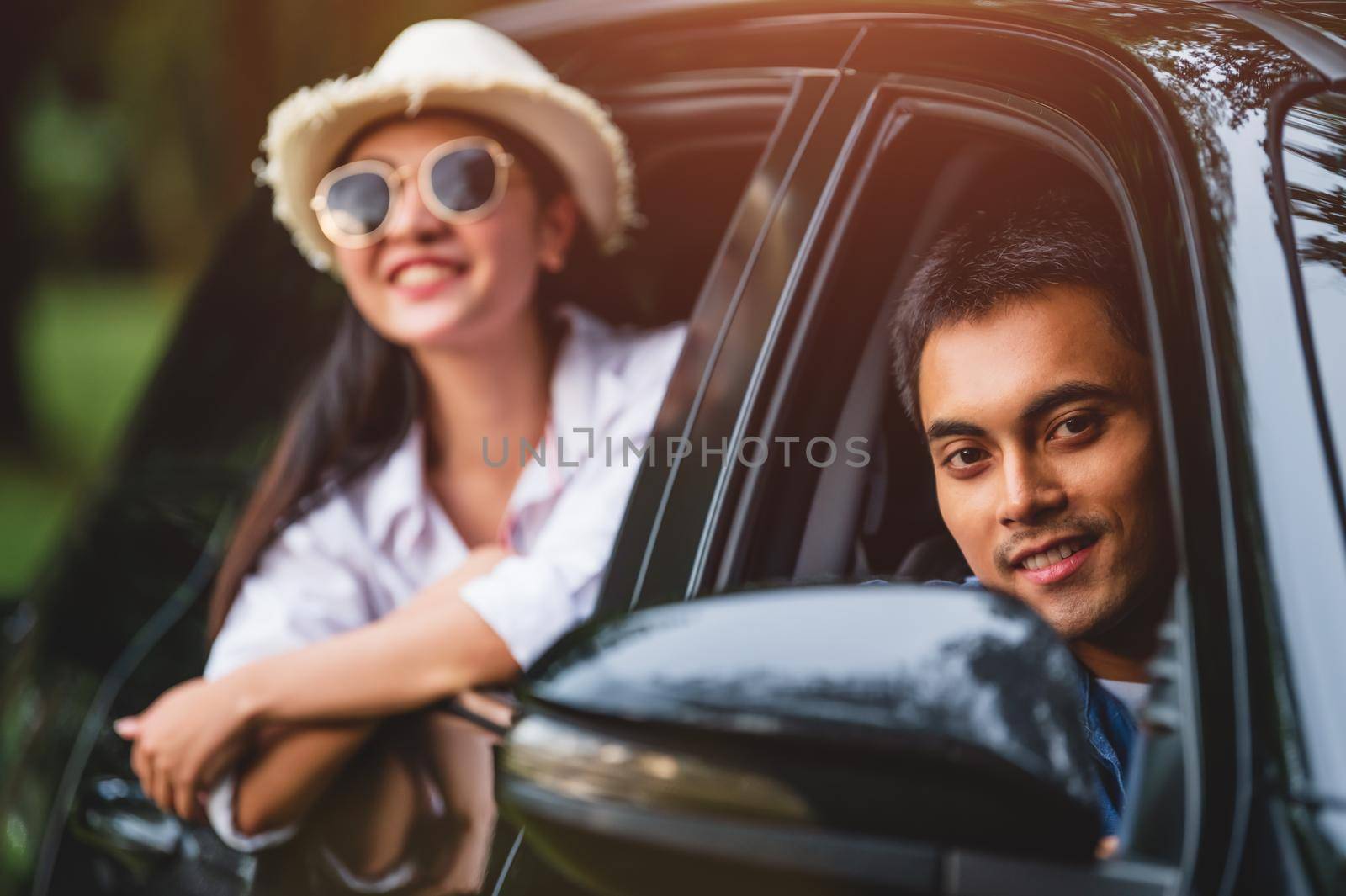 Happy Asian man looking outside open window car with his girlfriend on forest background. People lifestyle relax as traveler on road trip in holiday vacation. Transportation travel. Looking at camera