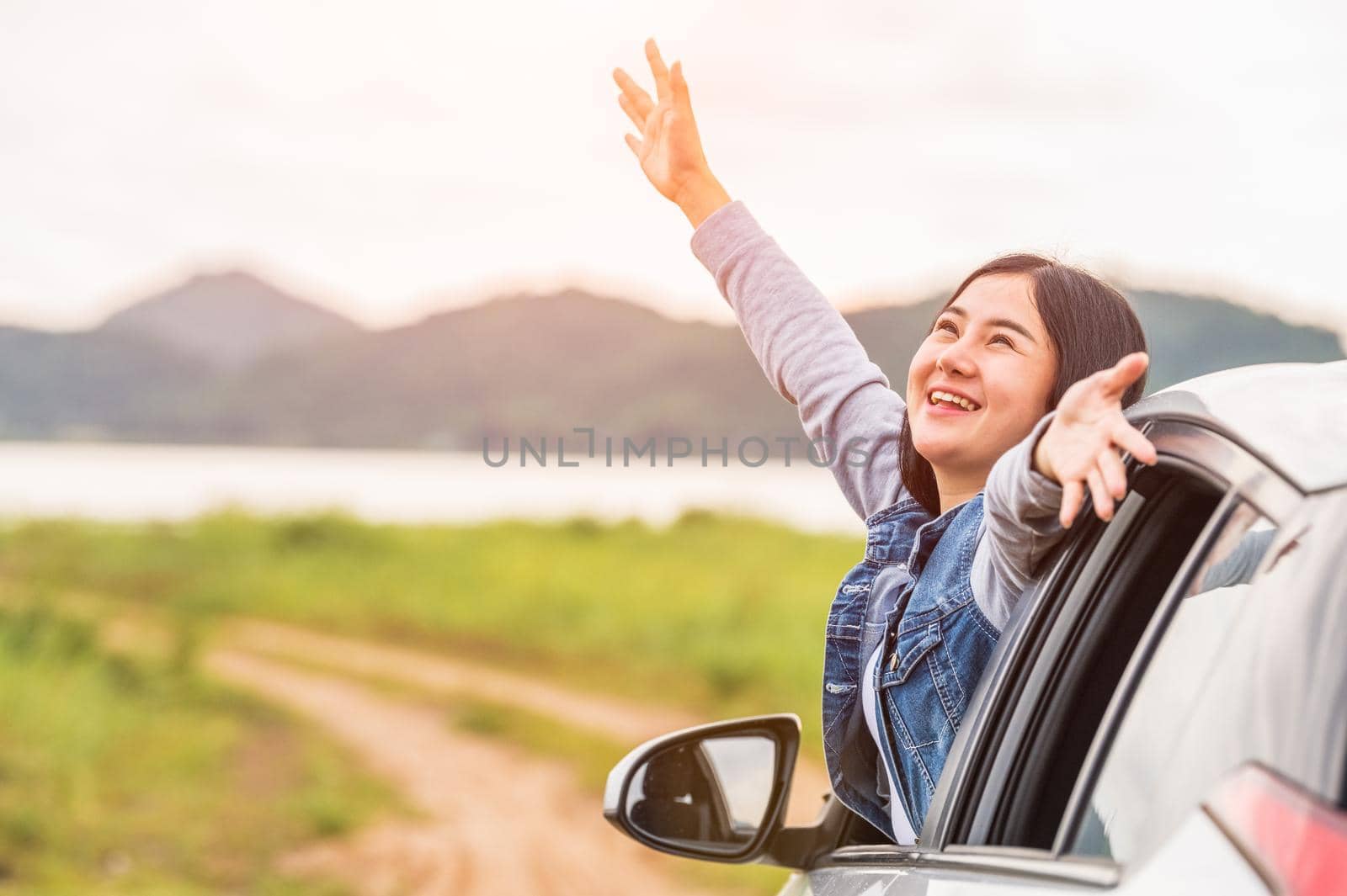 Happy Asian woman spread arms out of window under sunset at seaside with nature  background during travel in holiday. Confidence cheerful girl with dawn sky. Sun sea and mountain. Vacation concept