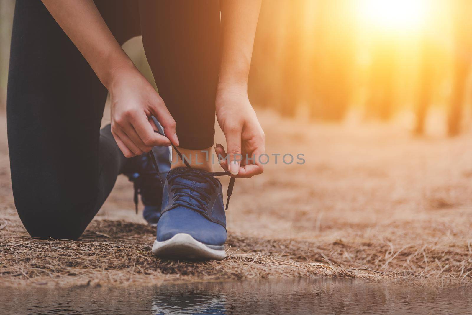 Young fitness running woman tying shoelaces at outdoors in forest background. Sport and Nature concept. Countryside Exercise and and Athlete Activity concept. Healthy and Lifestyle theme.