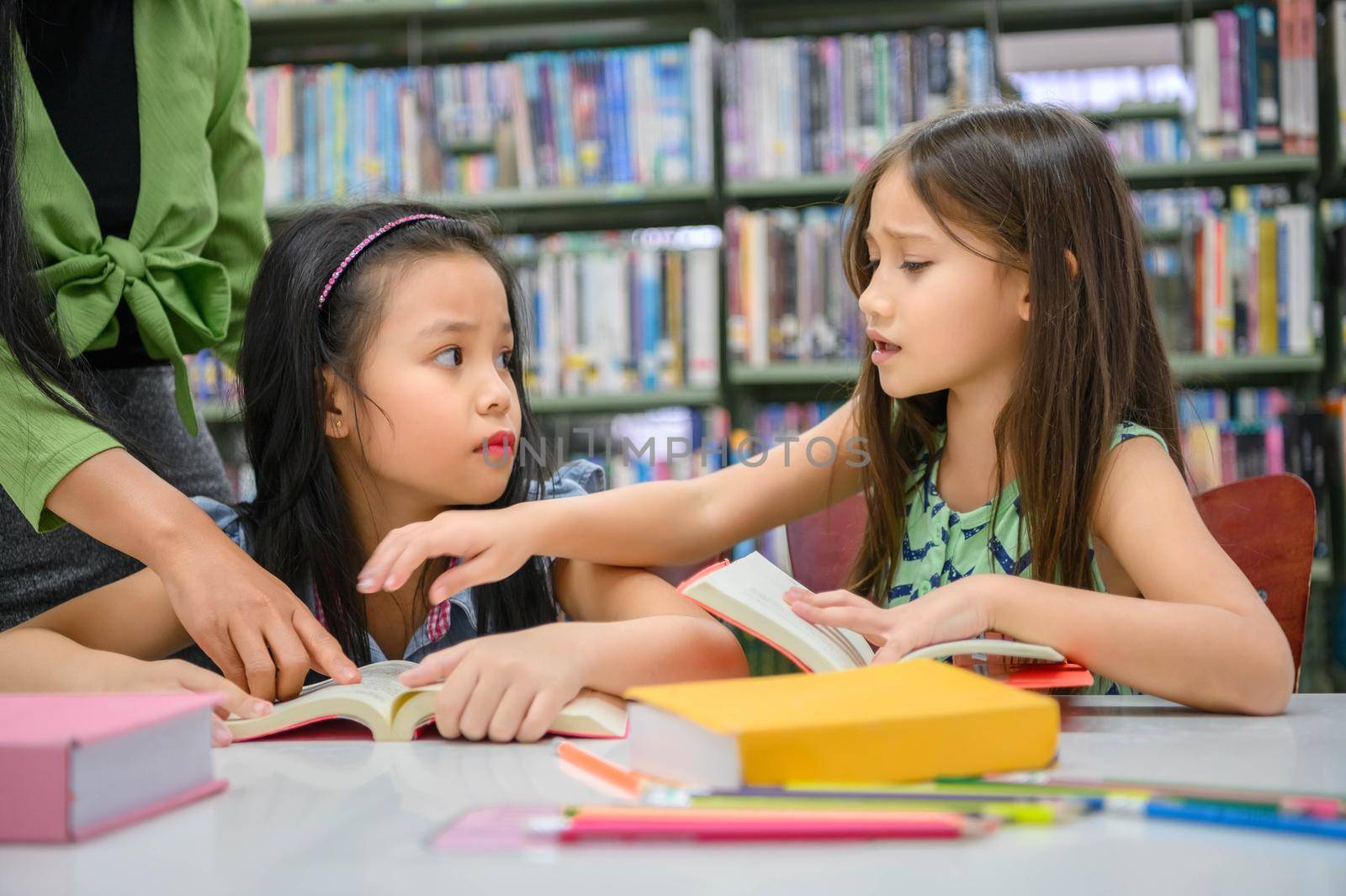 Two cute girls conflict while reading books in library when teacher teaching. People lifestyles and education. Young friendship and Kids relationship in school concept. Daycare theme