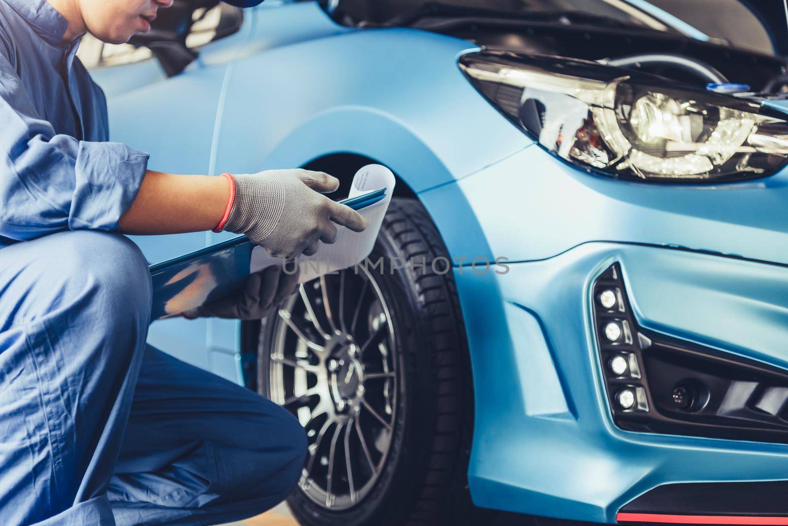 Asian car mechanic technician holding clipboard and checking to maintenance vehicle by customer claim order in auto repair shop garage. Wheel tire repair service. People occupation and business job