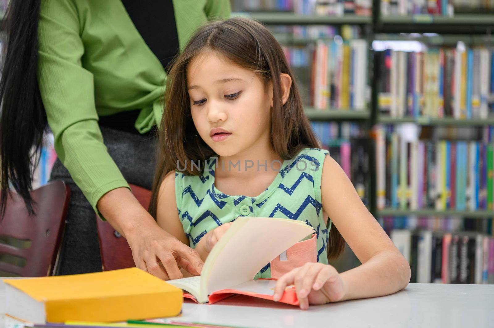 Girl ask for teacher to answer question in book while reading book at school library. Education and learning concept.