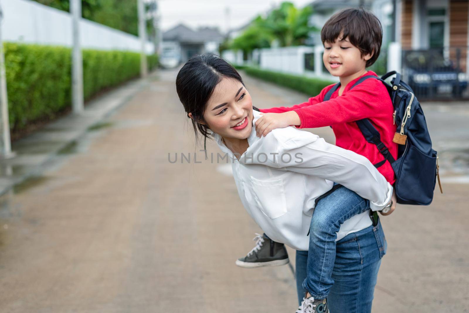 Single mom carrying and playing with her children near home with villa street background. People and Lifestyles concept. Happy family and Home sweet home theme. Outdoors and nature theme.