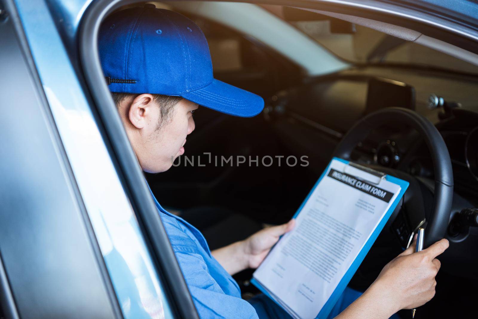 Mechanic holding clipboard and checking inside car to maintenance vehicle by customer claim order in auto repair shop garage. Repair service. People occupation and business job. Automobile technician