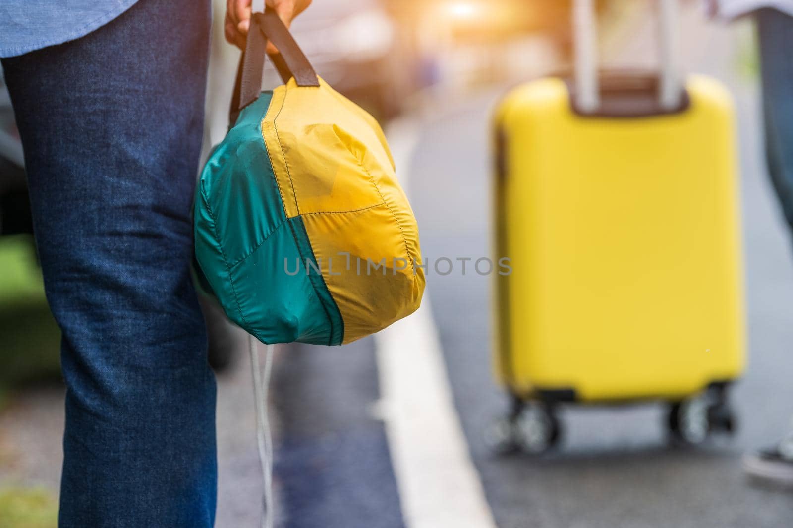 Closeup of tourist legs walking along road with bag during travel in countryside. People lifestyles and vacation concept. Man holding and backpacking for long holiday trip with mountain background