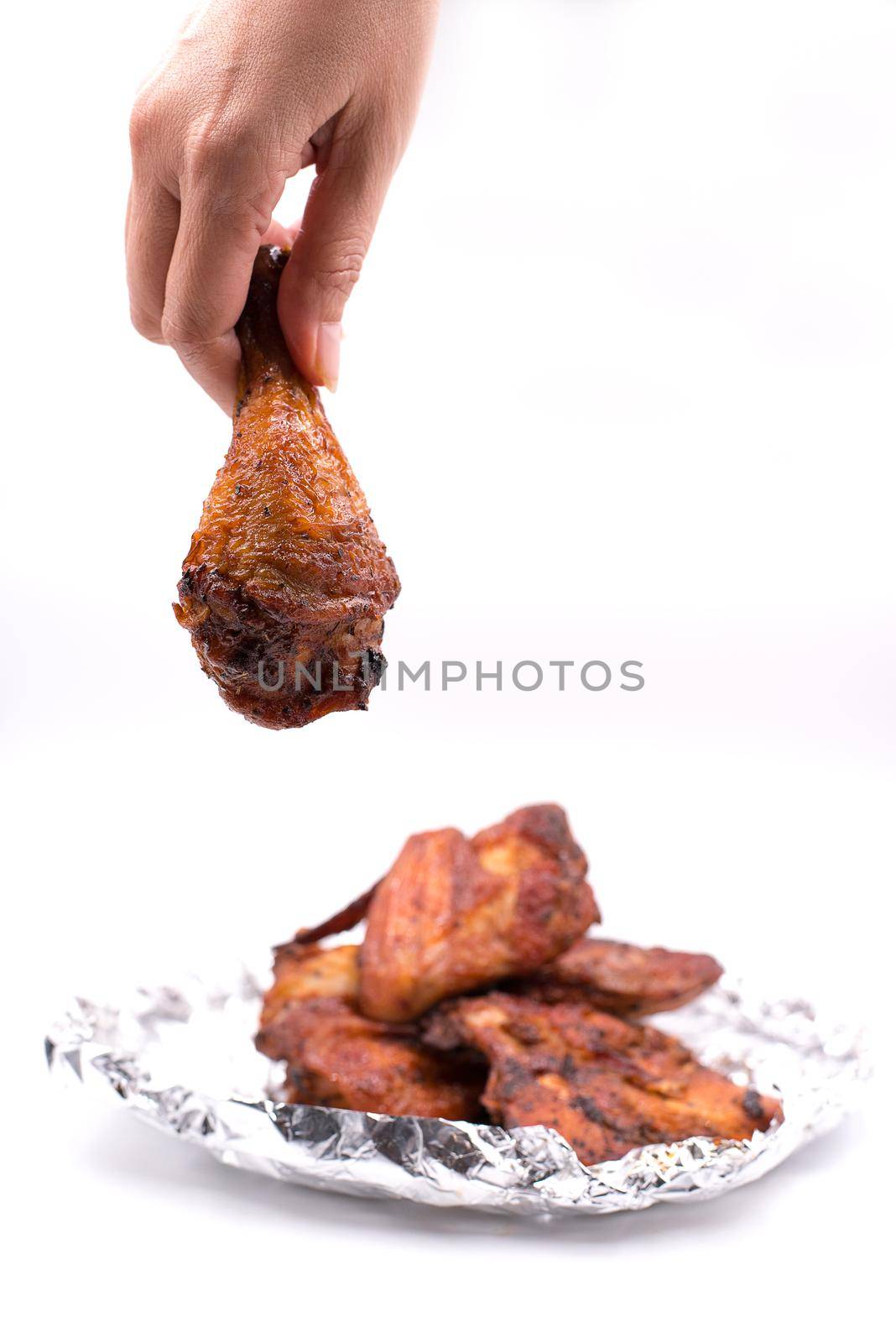 Hand catching roasted chicken leg. delicious grill chicken on foil on isolated white background. Food and appetizer concept by MiniStocker