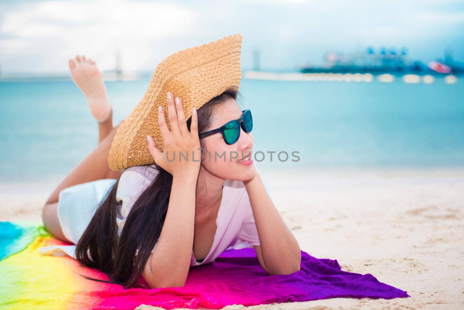 Asian woman in casual and straw hat lying on tropical beach with sea background. Relax and lifestyle concept. Holiday and Vacation concept. Single woman and happiness theme.