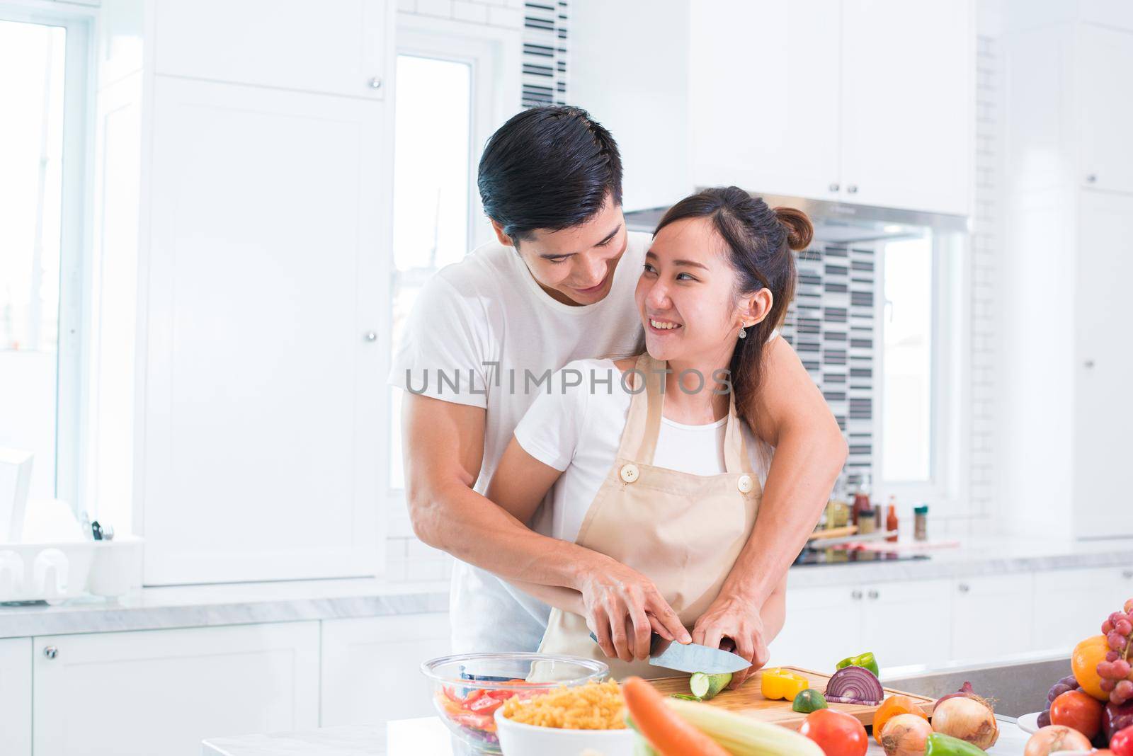Asian lovers or couple cooking and slicing vegetable in kitchen room. Man and woman looking each other in home. Holiday and Honeymoon concept. Valentine day and wedding theme