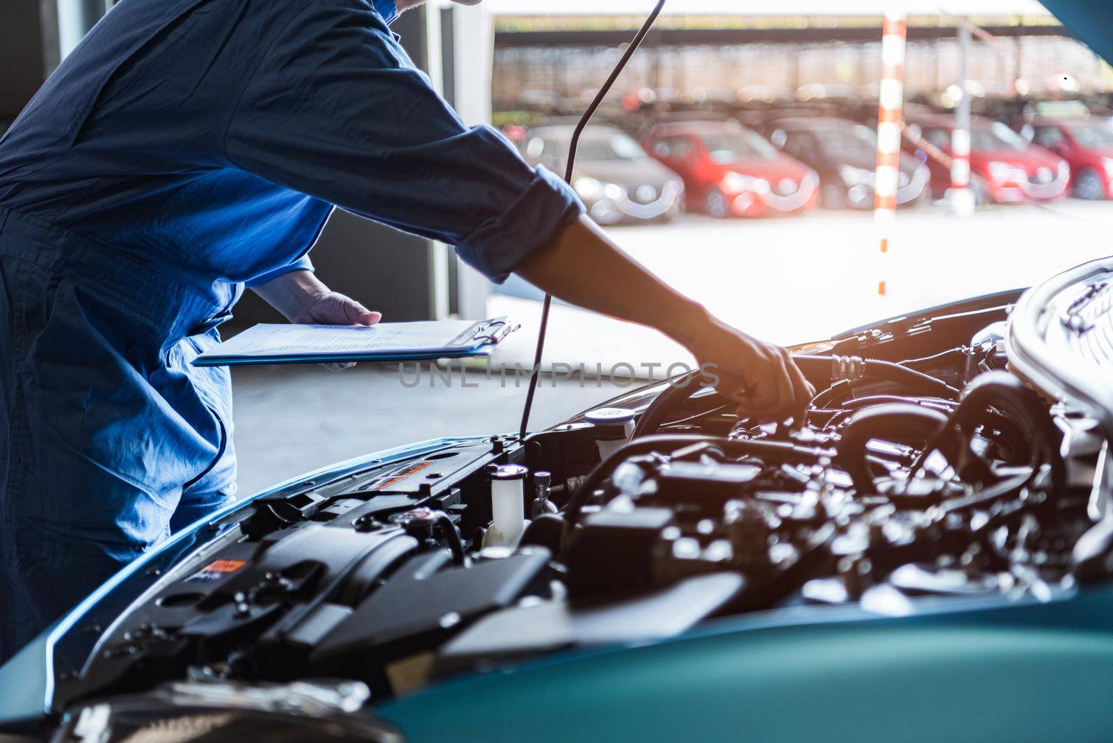 Car mechanic holding clipboard and checking to maintenance vehicle by customer claim order in auto repair shop garage. Engine repair service. People occupation and business job. Automobile technician