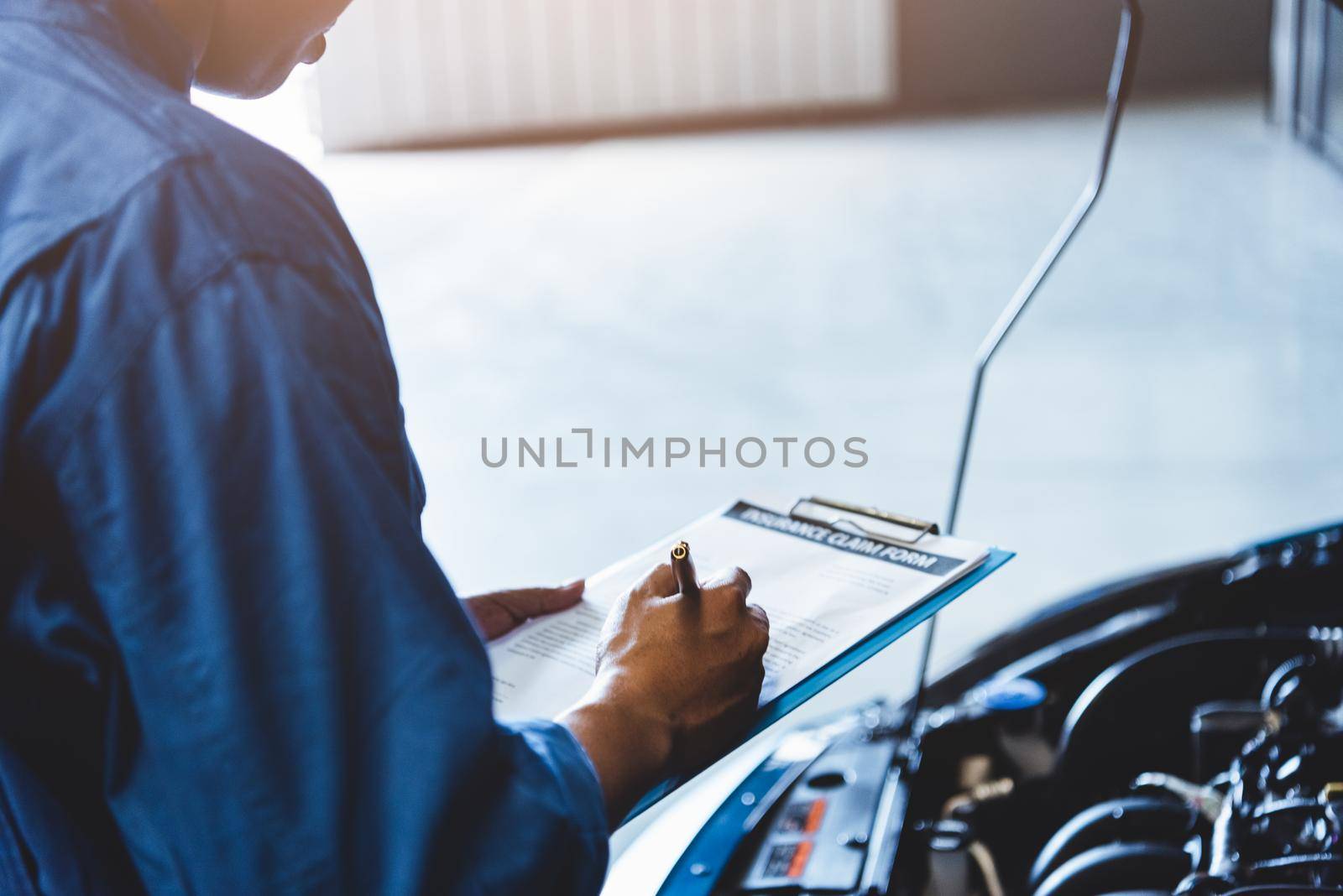 Car mechanic holding clipboard and checking to maintenance vehicle by customer claim order in auto repair shop garage. Engine repair service. People occupation and business job. Automobile technician