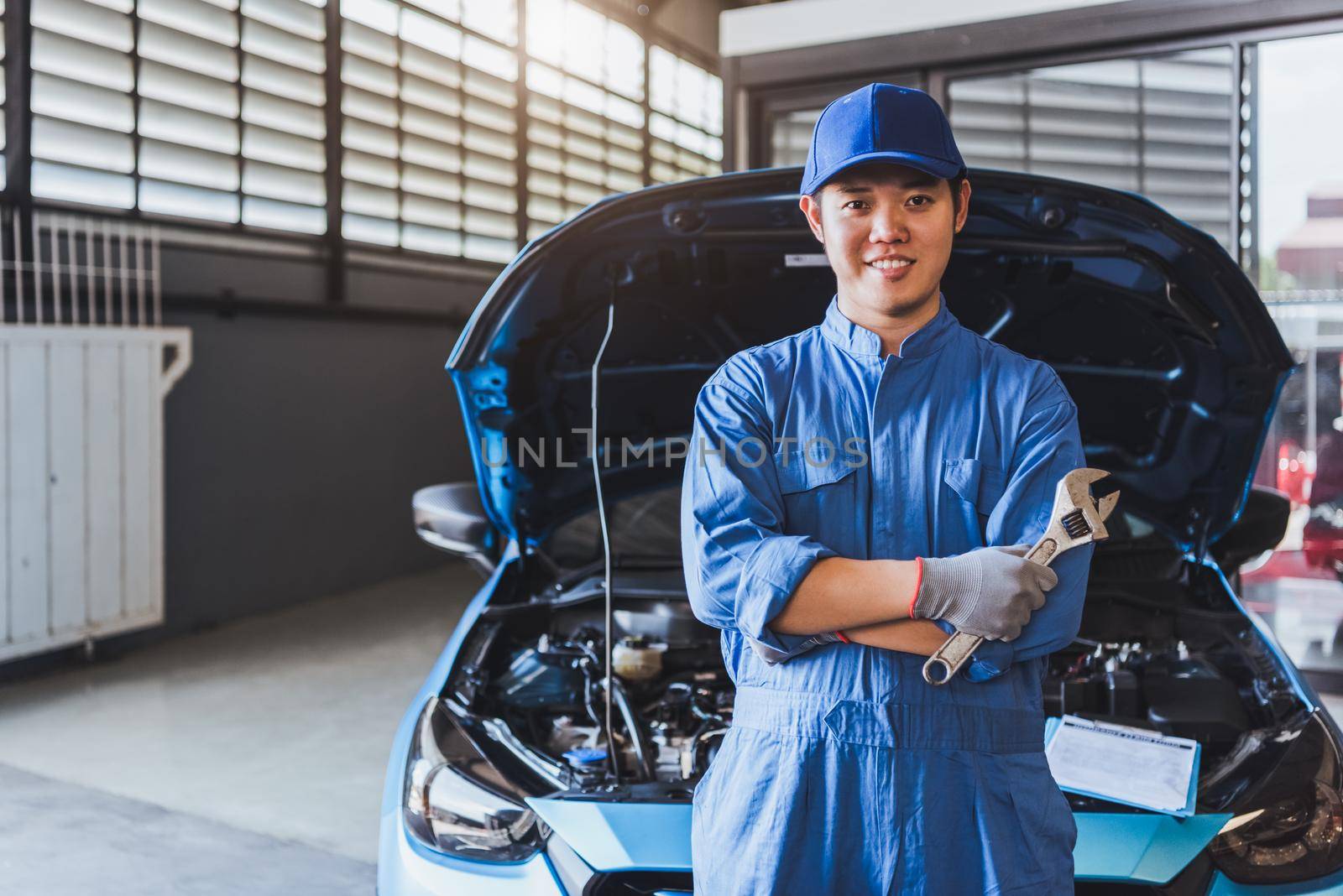 Happy car mechanic inspection technician holding wrench and smiling to camera after fixing customer car claim in service maintenance insurance of car engine. Transportation automotive industry concept