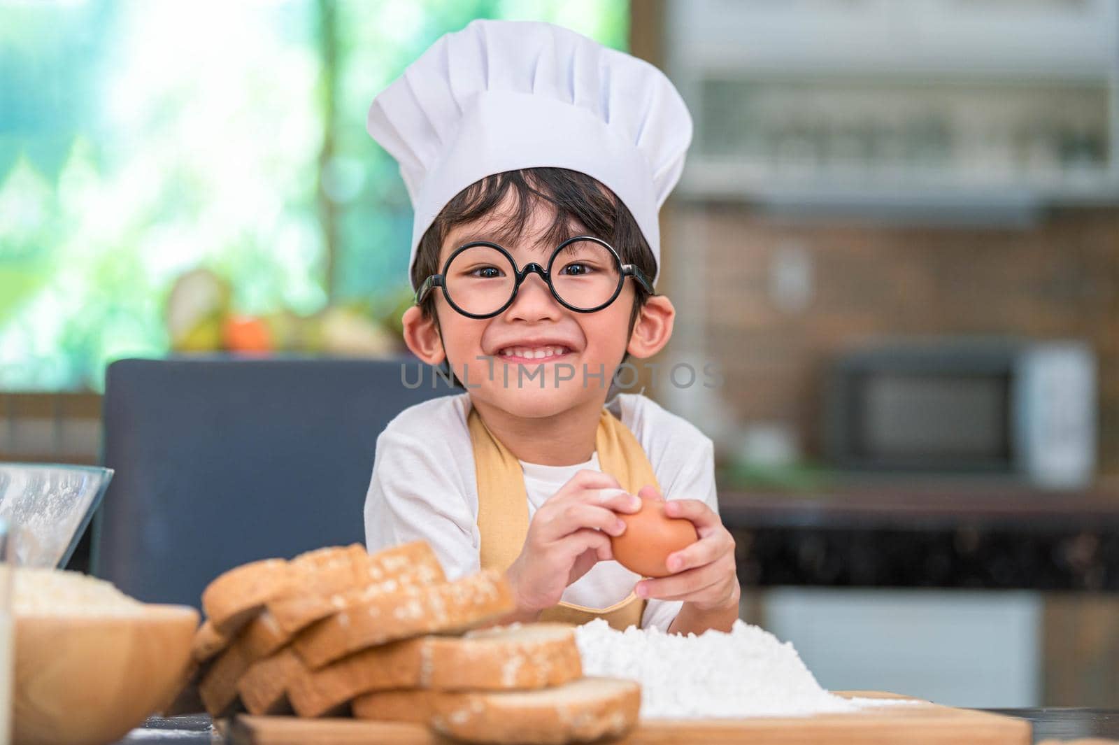 Portrait cute little Asian happy boy interested in cooking funny in home kitchen. People lifestyles and Family. Homemade food and ingredients concept. Baking Christmas cake and cookies. Smiling child