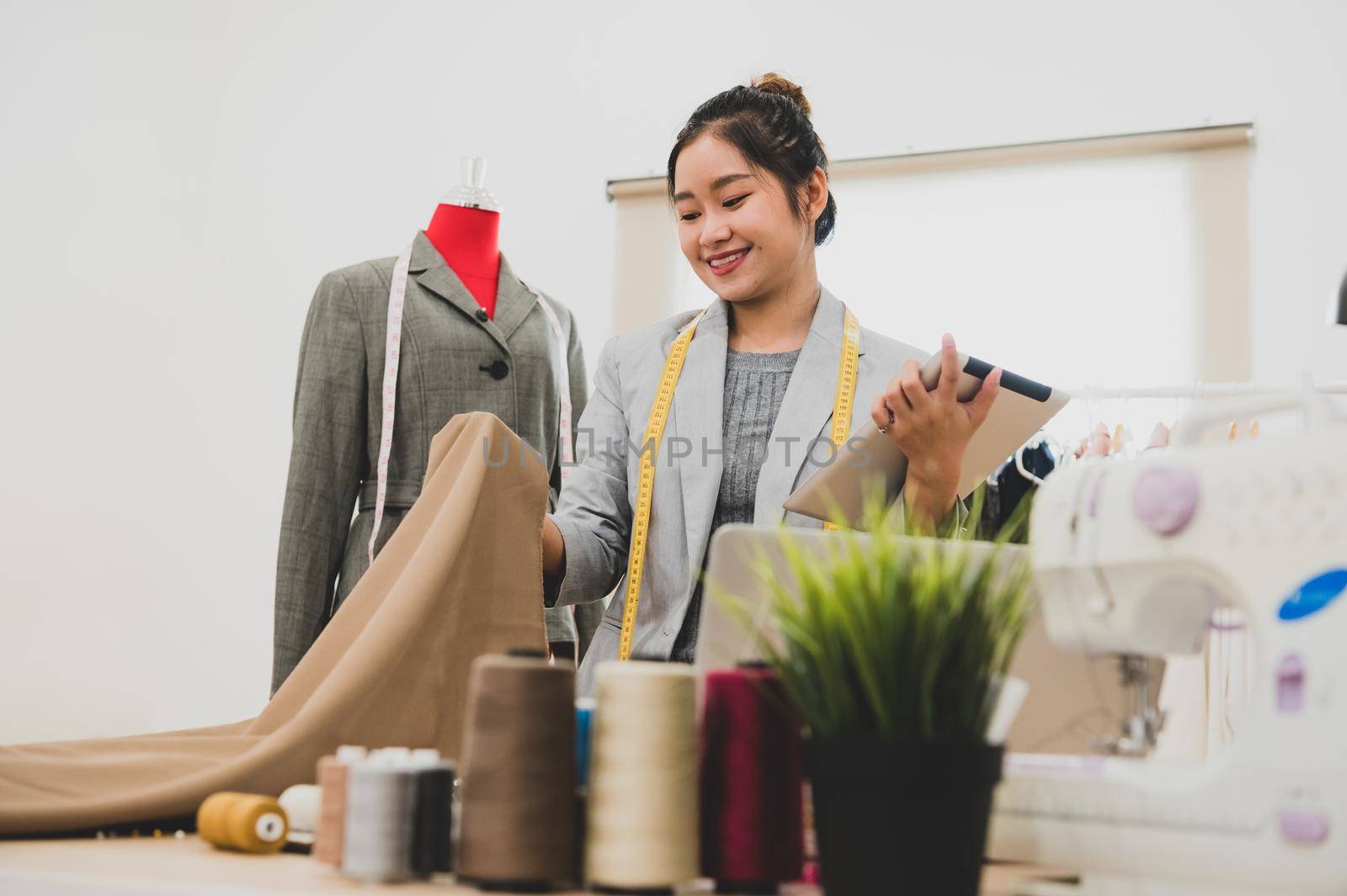 Fashion designer stylist in business owner workshop with tablet and customer contact list. Tailor and sew concept. Portrait of happy casual trendy fashion businesswoman in studio. Job and occupation
