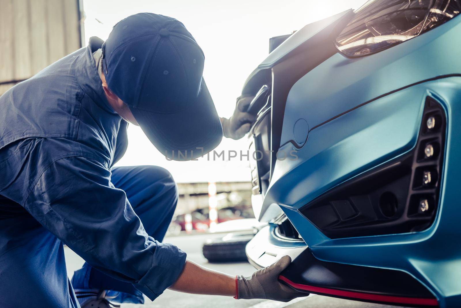 Mechanics installing front skirt at auto repair shop garage. Transportation and Business concept. Automobile technician maintenance vehicle by customer claim order. Car salon accessories decoration