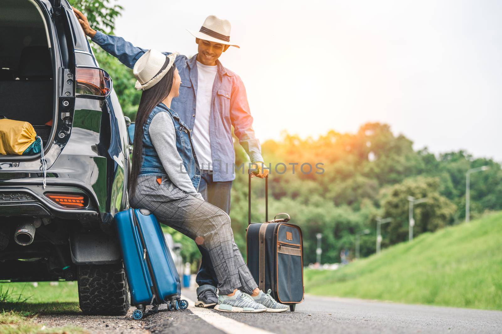 Closeup lower body of Asian couple relaxing on SUV car trunk with yellow trolly luggage along road trip with mountain hill background. Freedom road life. People lifestyle and transportation travel by MiniStocker