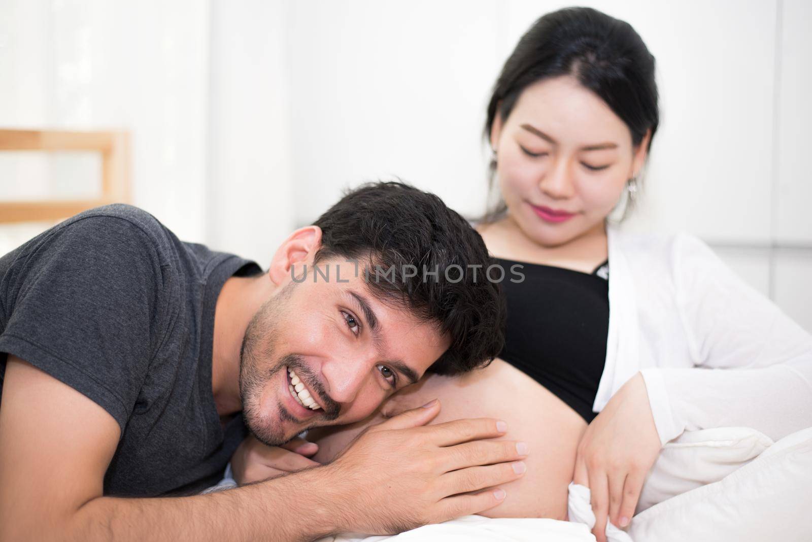 Father hearing his son or daughter kicking sound check inside mother belly when sitting on lying on bed at home. Family healthy and couples concept. Happy sweet home honeymoon and wedding theme