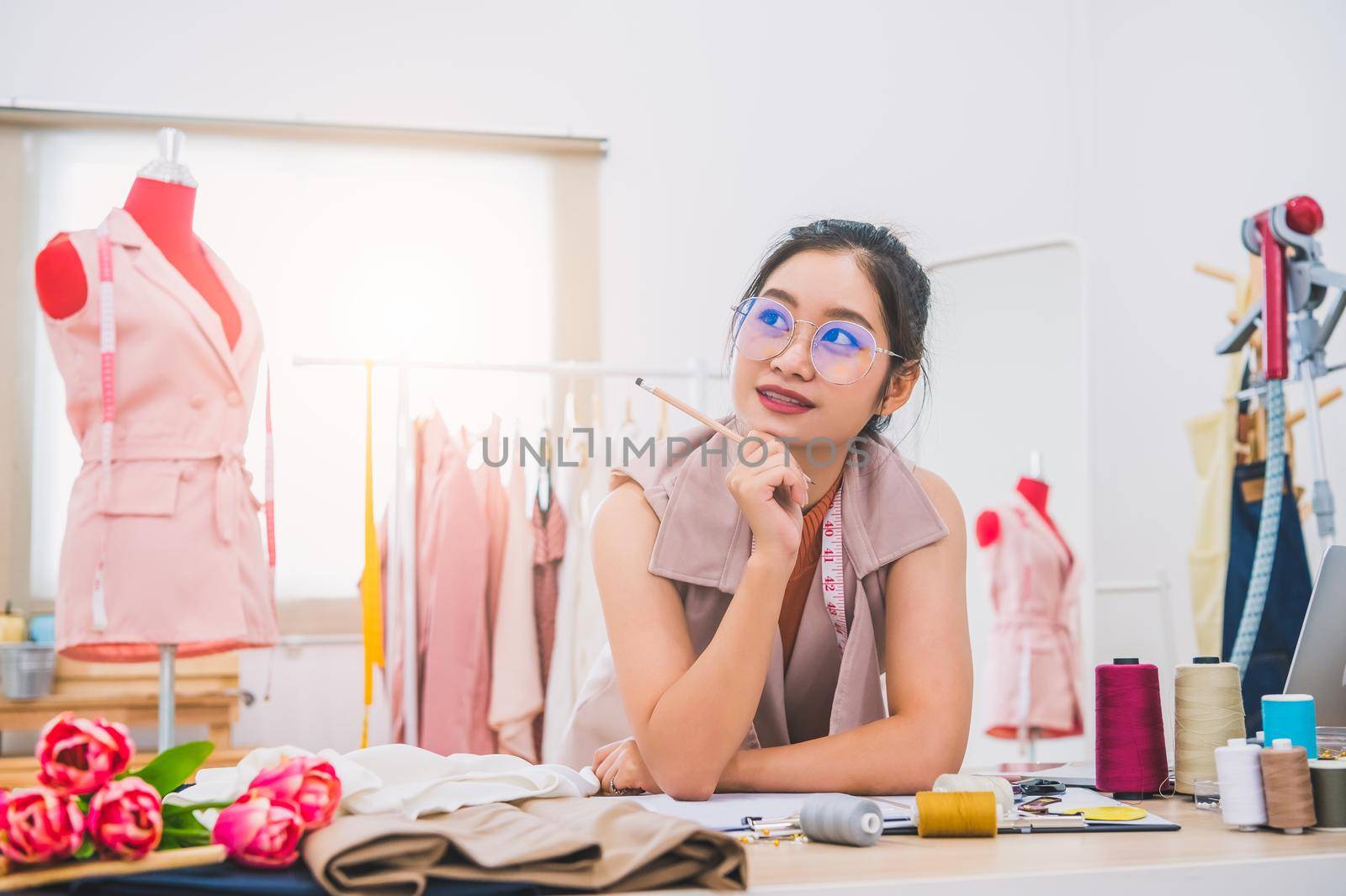 Attractive Asian female fashion designer working in home office workshop. Stylish fashionista woman creating new cloth design collection. Tailor and sewing. People lifestyle and occupation concept
