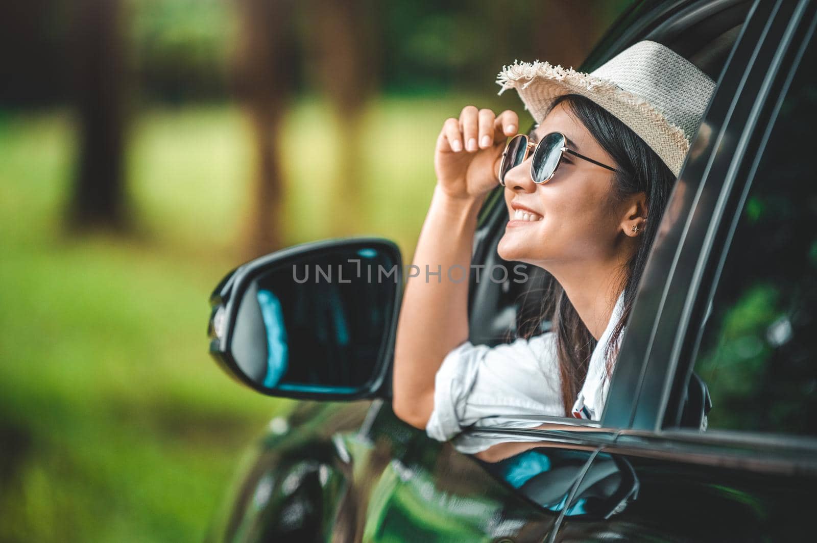 Happy woman hand holding hat outside open window car with green forest woods mountain background. People lifestyle relaxing as traveler on road trip in holiday vacation. Transportation and travel