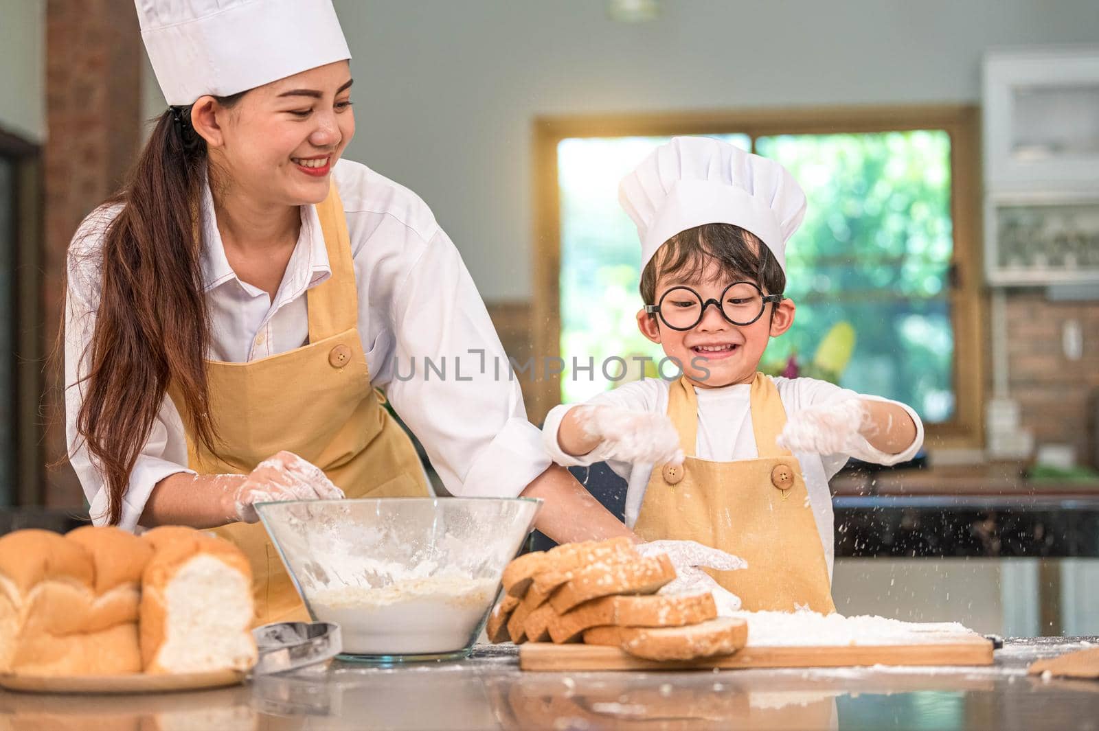 Cute little Asian boy and beautiful mother sifting dough flour with sifter sieve colander in home kitchen on table for prepare to baking bakery and cake. Thai kids playing with flour as chef funny