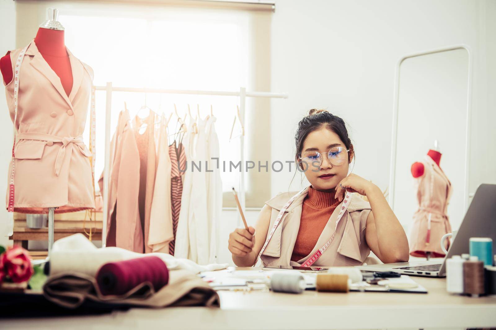 Attractive Asian female fashion designer working in home office workshop. Stylish fashionista woman creating new cloth design collection. Tailor and sewing. People lifestyle and occupation concept