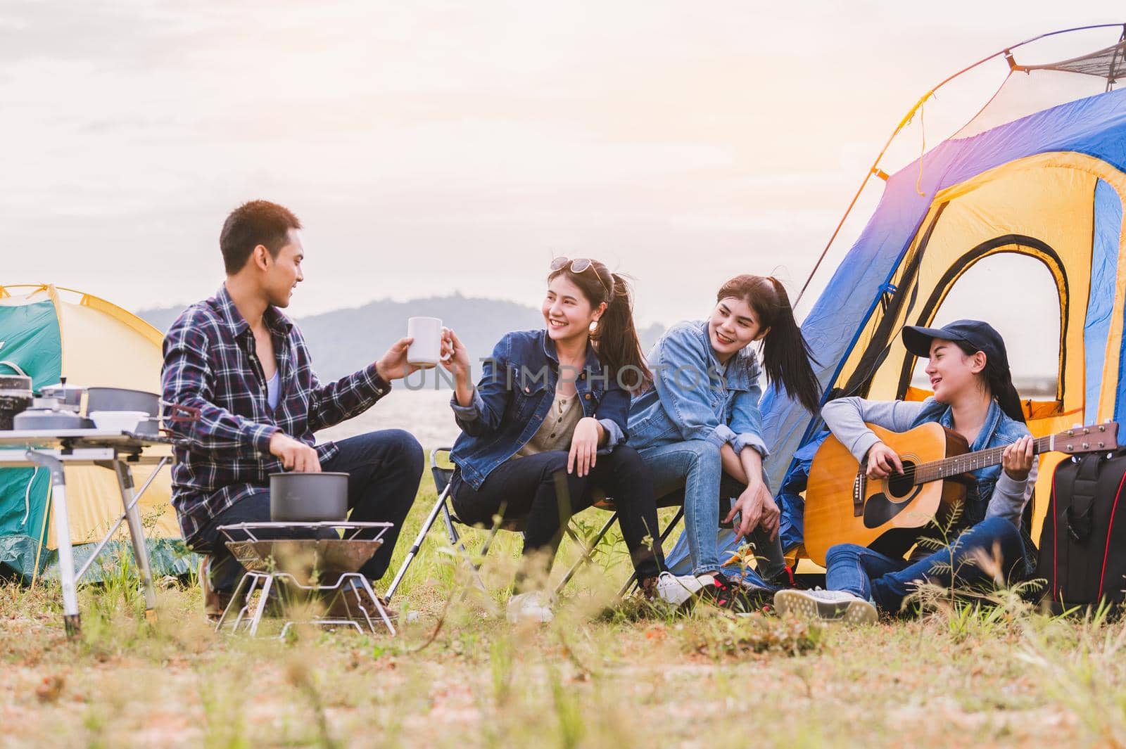 Group of Asian friendship clinking drinking bottle glass for celebrating in private party with mountain and lake view background. People lifestyle travel on vacation concept. Picnic and camping tent