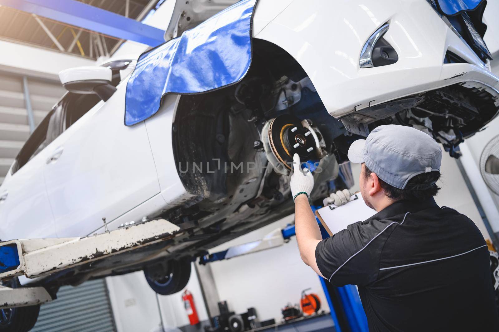 Asian male car technician car maintenance for customers according to specified vehicle maintenance checklist. Disk brake pad wear automotive repairing on vehicle. Safety inspection check service