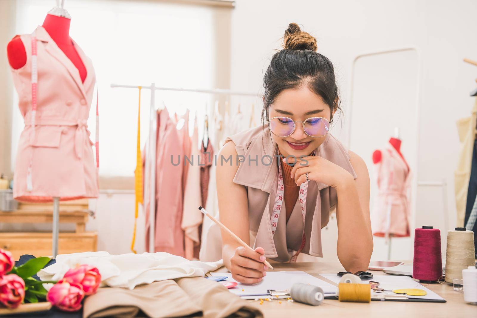Attractive Asian female fashion designer working in home office workshop. Stylish fashionista woman creating new cloth design collection. Tailor and sewing. People lifestyle and occupation concept
