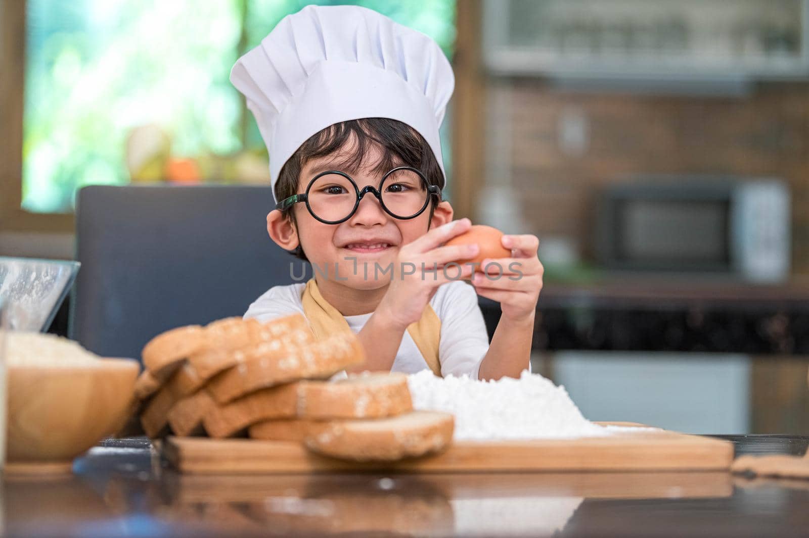 Portrait cute little Asian happy boy interested in cooking funny in home kitchen. People lifestyles and Family. Homemade food and ingredients concept. Baking Christmas cake and cookies. Smiling child