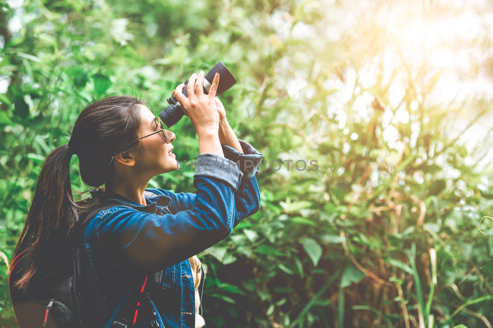 Beautiful Asian woman with binoculars telescope in forest looking destination. People lifestyles and leisure activity. Nature and backpacker traveling jungle background. Bird watching and living
