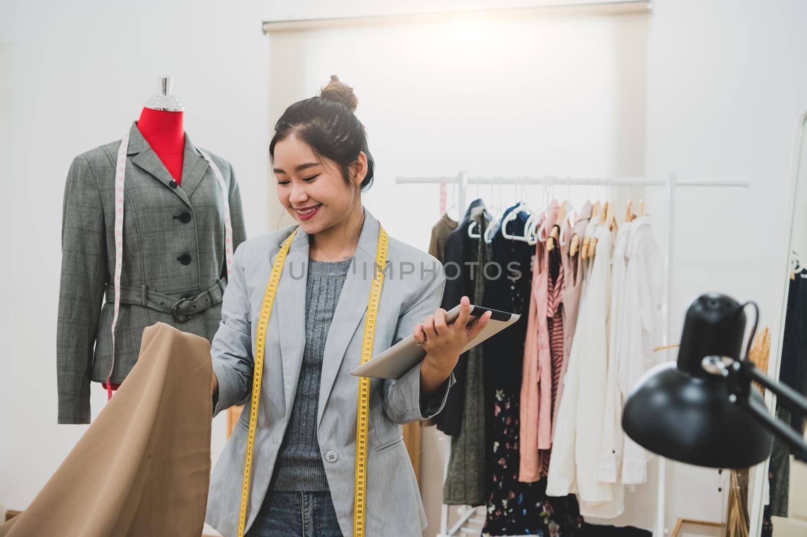 Fashion designer stylist in business owner workshop with tablet and customer contact list. Tailor and sew concept. Portrait of happy casual trendy fashion businesswoman in studio. Job and occupation