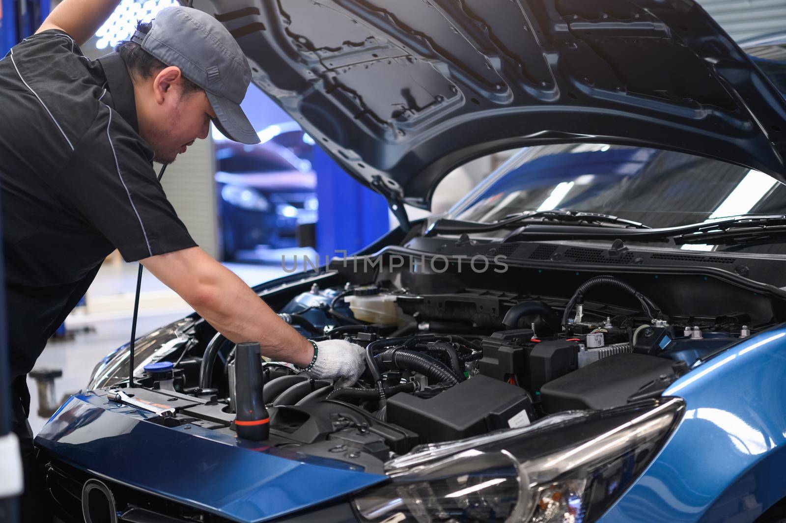 Asian male auto mechanic examine car engine breakdown problem in front of automotive vehicle car hood. Safety technical inspection care check service maintenance for customer before long road trip