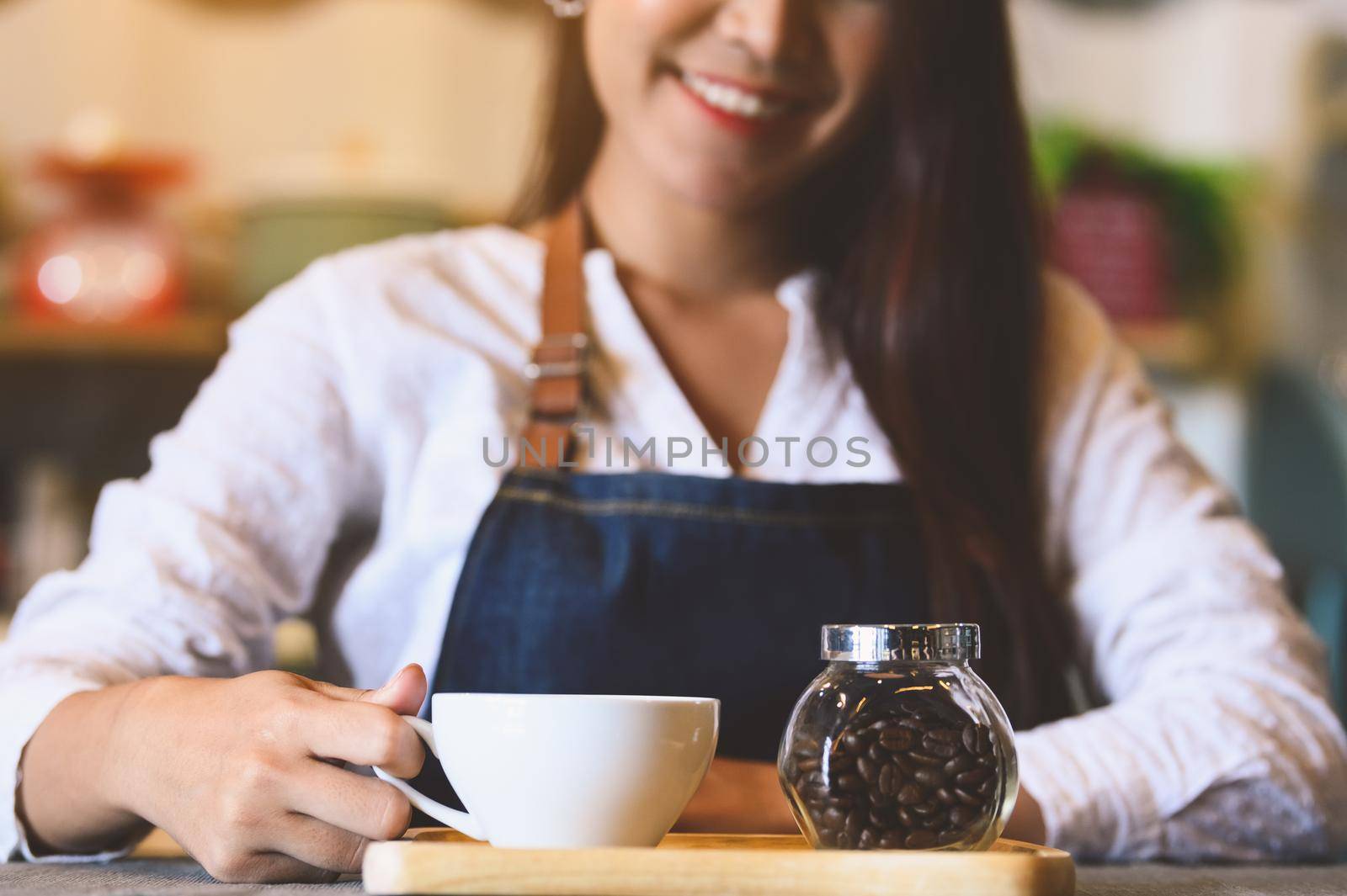 Closeup of white coffee cup with beautiful Asian woman barista background for serving to customer. Job and occupation. Food and drink beverage. Coffee shop and Cafe. Business and restaurant ownership