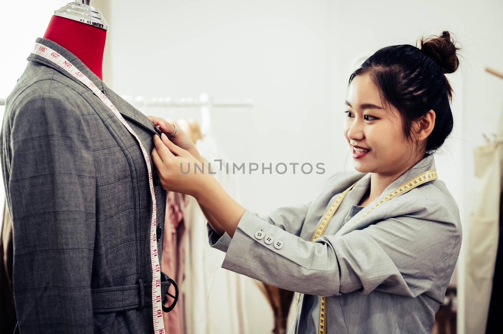 Asian female fashion designer girl making fit on the formal suit uniform clothes on mannequin model. Fashion designer stylish showroom. Sewing and tailor concept. Creative dressmaker stylist.