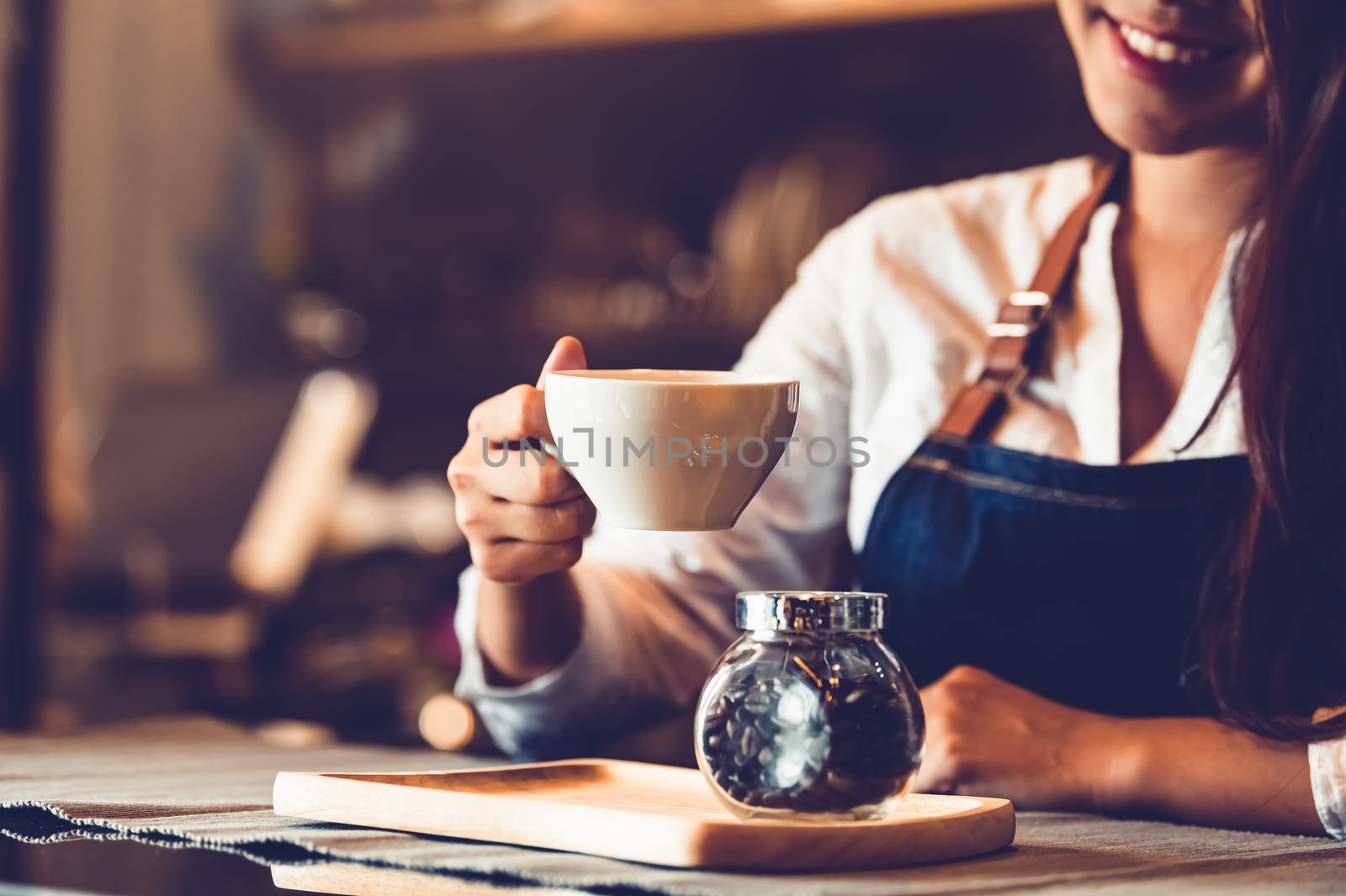 Closeup of professional female barista hand making and holding white cup of coffee. Happy young woman at counter bar in restaurant background. People lifestyles and Business occupation concept