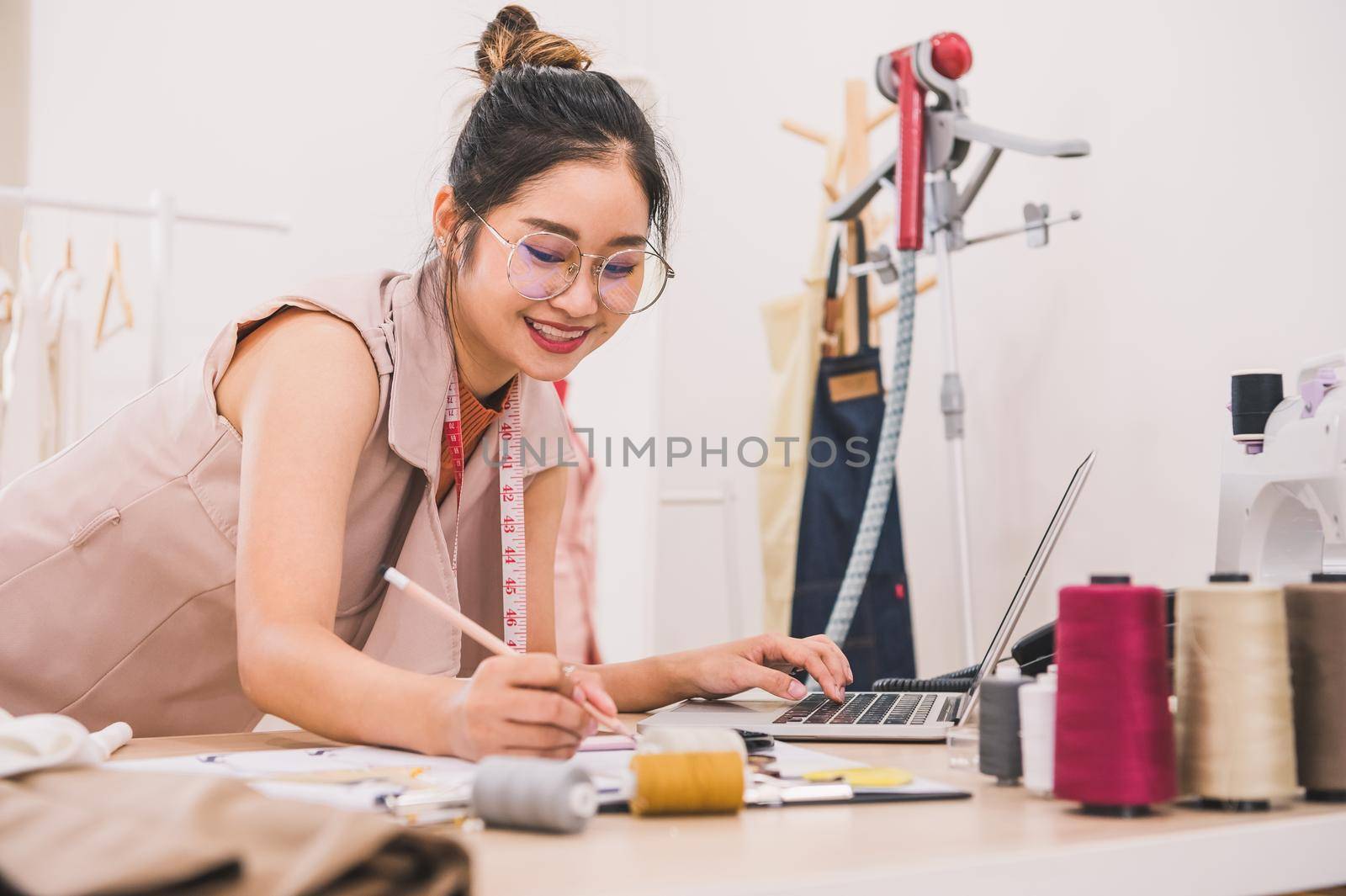 Attractive Asian female fashion designer working in home office workshop. Stylish fashionista woman creating new cloth design collection. Tailor and sewing. People lifestyle and occupation concept