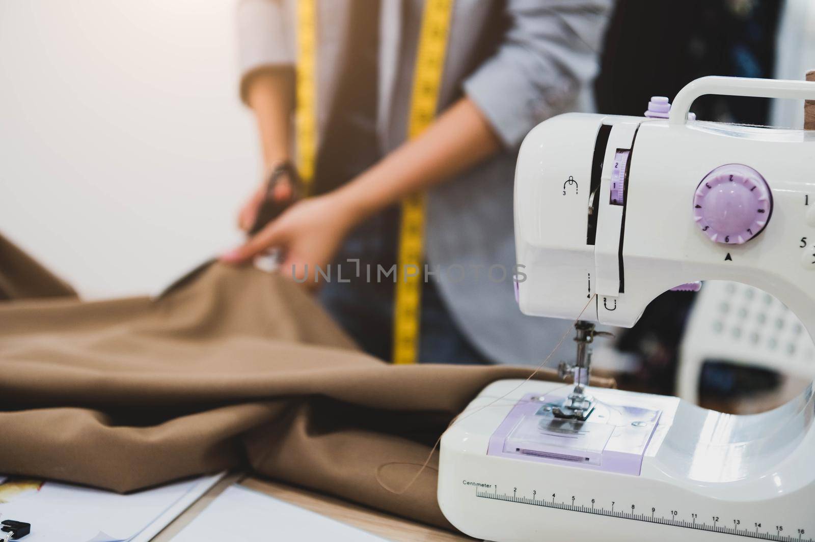 Dressmaker cutting dress fabric on sketch line with sewing machine foreground. Fashion designer tailor or sewer in workshop studio designing new collection clothes. Business owner and entrepreneur