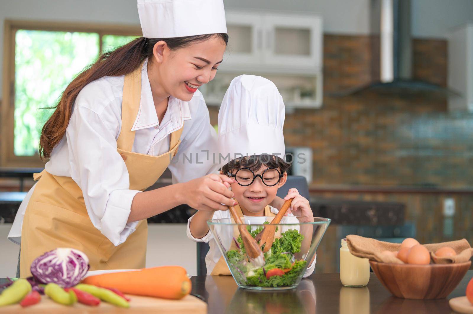 Happy beautiful Asian woman and cute little boy with eyeglasses prepare to cooking in kitchen at home. People lifestyles and Family. Homemade food and ingredients concept. Two Thai people life