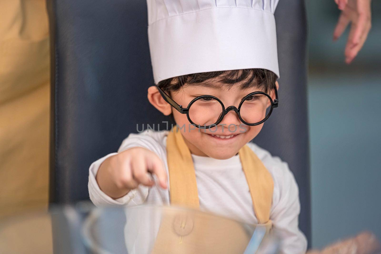 Portrait cute little Asian happy boy interested in cooking with mother funny in home kitchen. People lifestyles and Family. Homemade food and ingredients concept. Baking Christmas cake and cookies