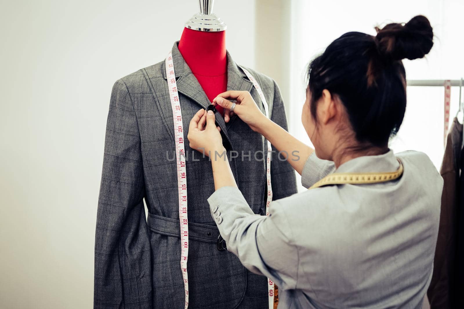 Asian female fashion designer girl making fit on the formal suit uniform clothes on mannequin model. Fashion designer stylish showroom. Sewing and tailor concept. Creative dressmaker stylist.